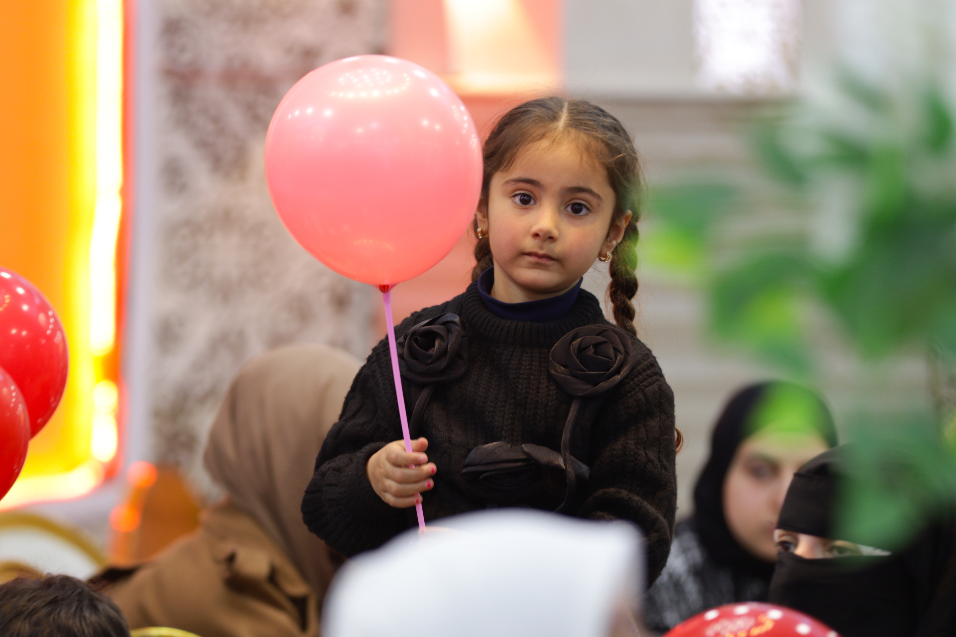 A young girl holding a pink balloon, looking at the camera