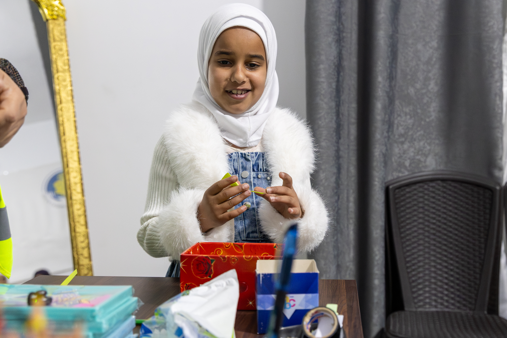 A girl in a hijab doing crafts at a desk with a gift box