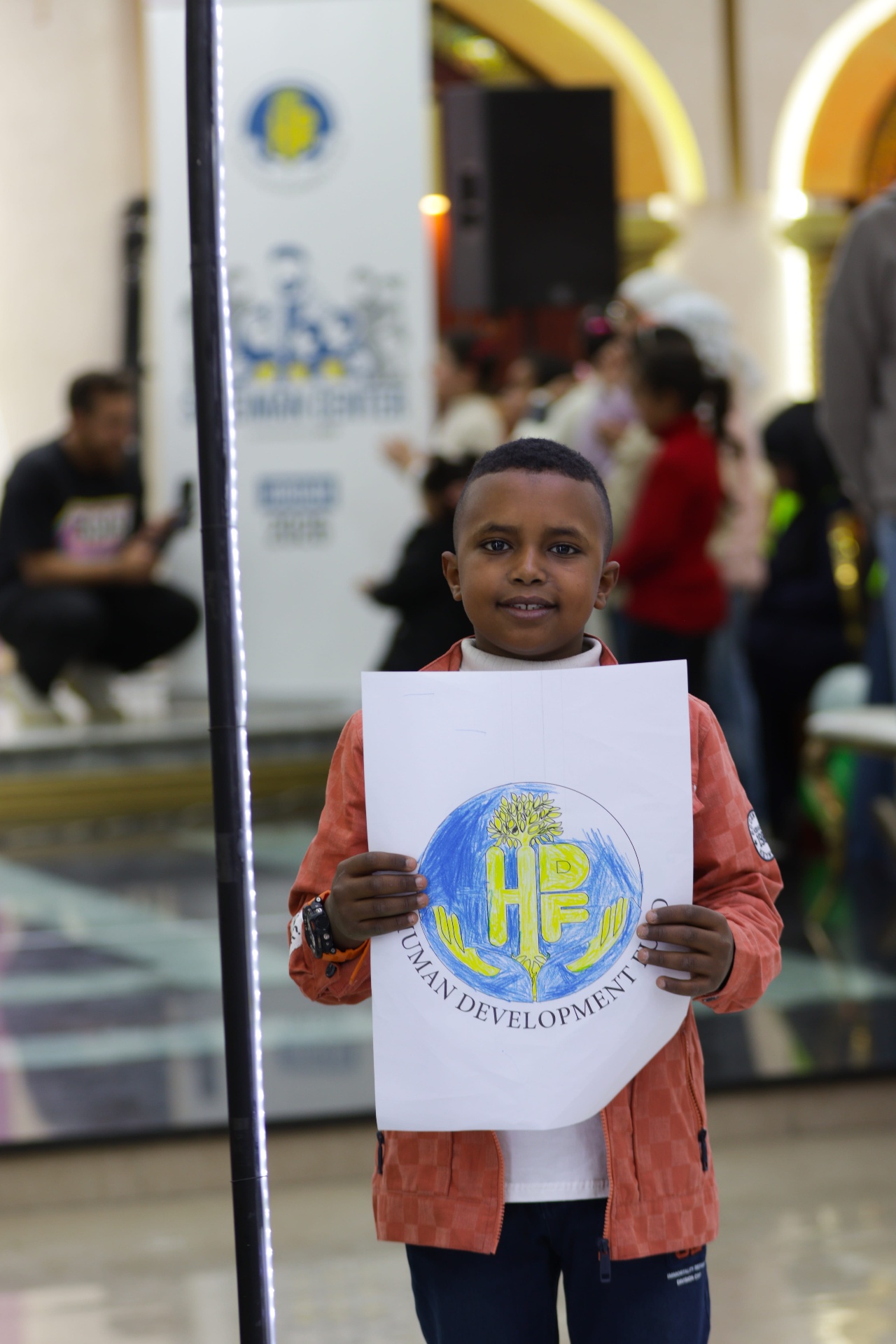 A boy holding up his own hand-colored drawing of the HDF logo