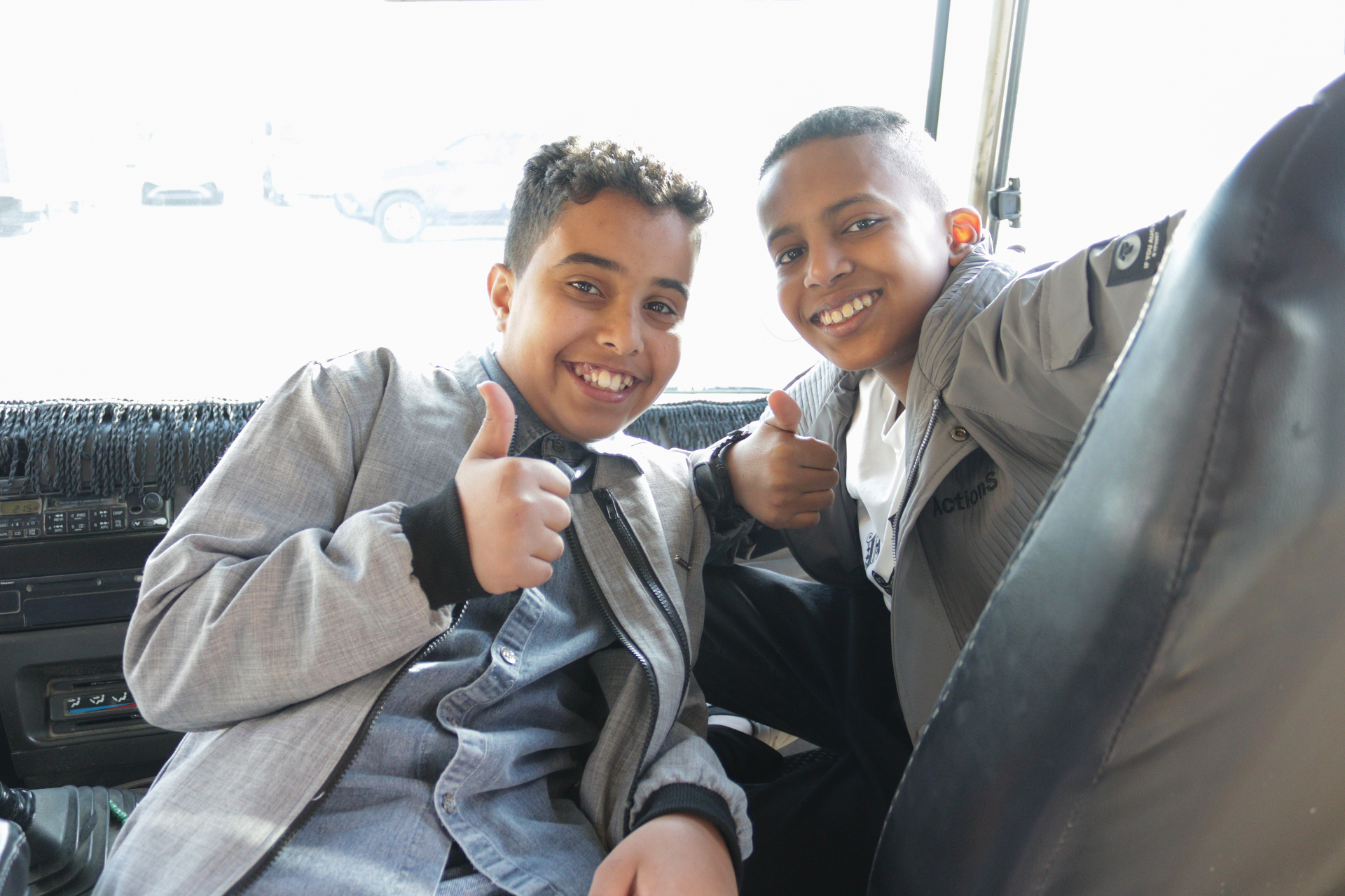 Two boys in the back of a car, both giving thumbs up and smiling